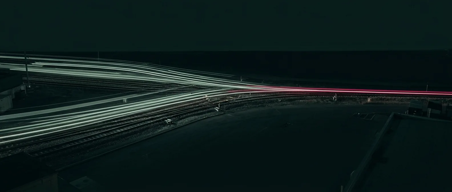 Long-exposure light trails merging through a rail junction into a single track